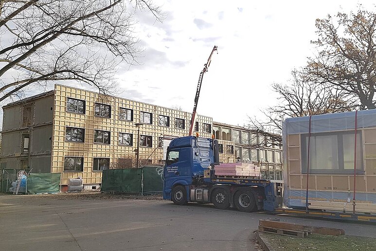 LKW mit Kran und fliegenden Fassadenteilen vor Verwaltungsgebäude