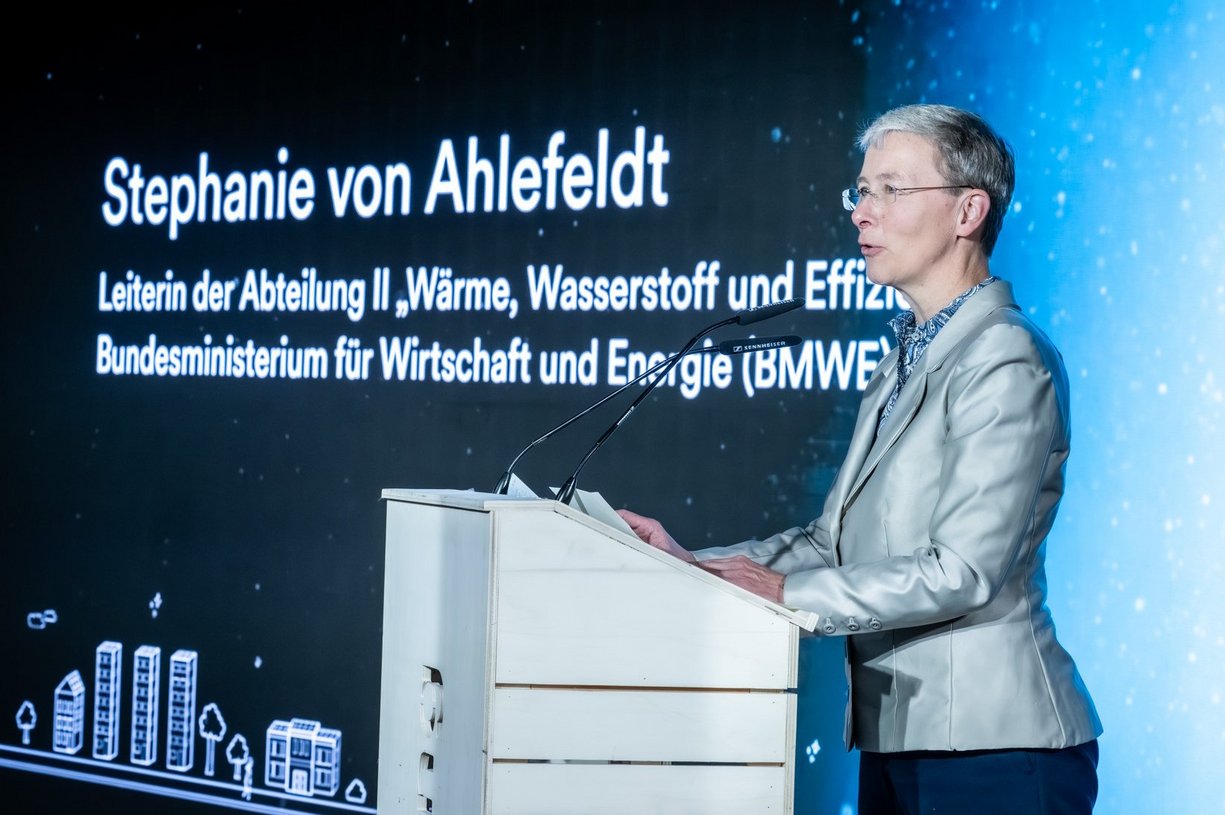 Person steht hinter Rednerpult und spricht, im Hintergrund eine Projektionsfläche.