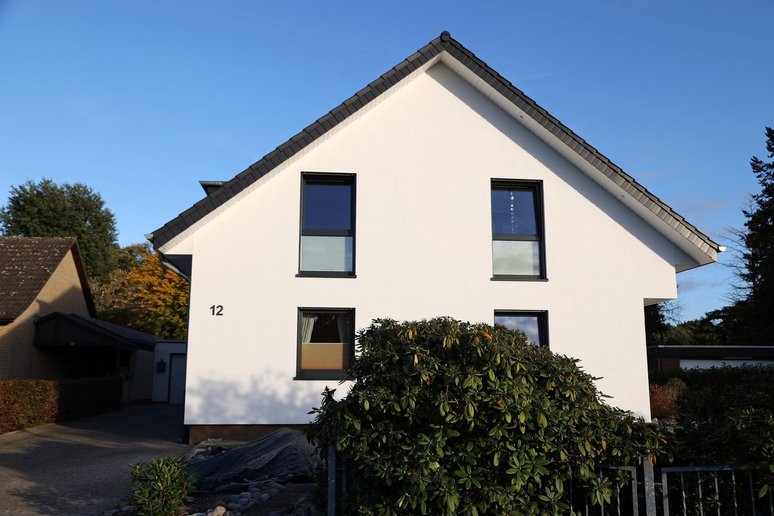 Hausfassade mit Garten davor wird von der Sonne angestrahlt