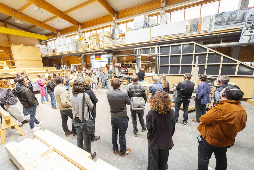 Bild zeigt: Menschengruppe steht in einer Werkshalle vor einer vorgefertigten Fassade