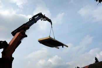 Bild zeigt Kran mit fliegender Fassade vor bewölktem Himmel