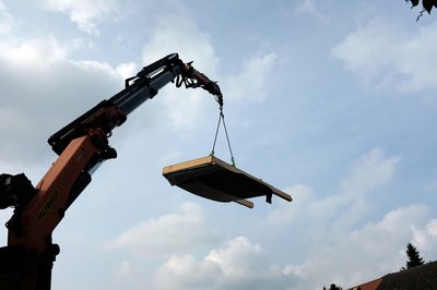 Bild zeigt Kran mit fliegender Fassade vor bewölktem Himmel
