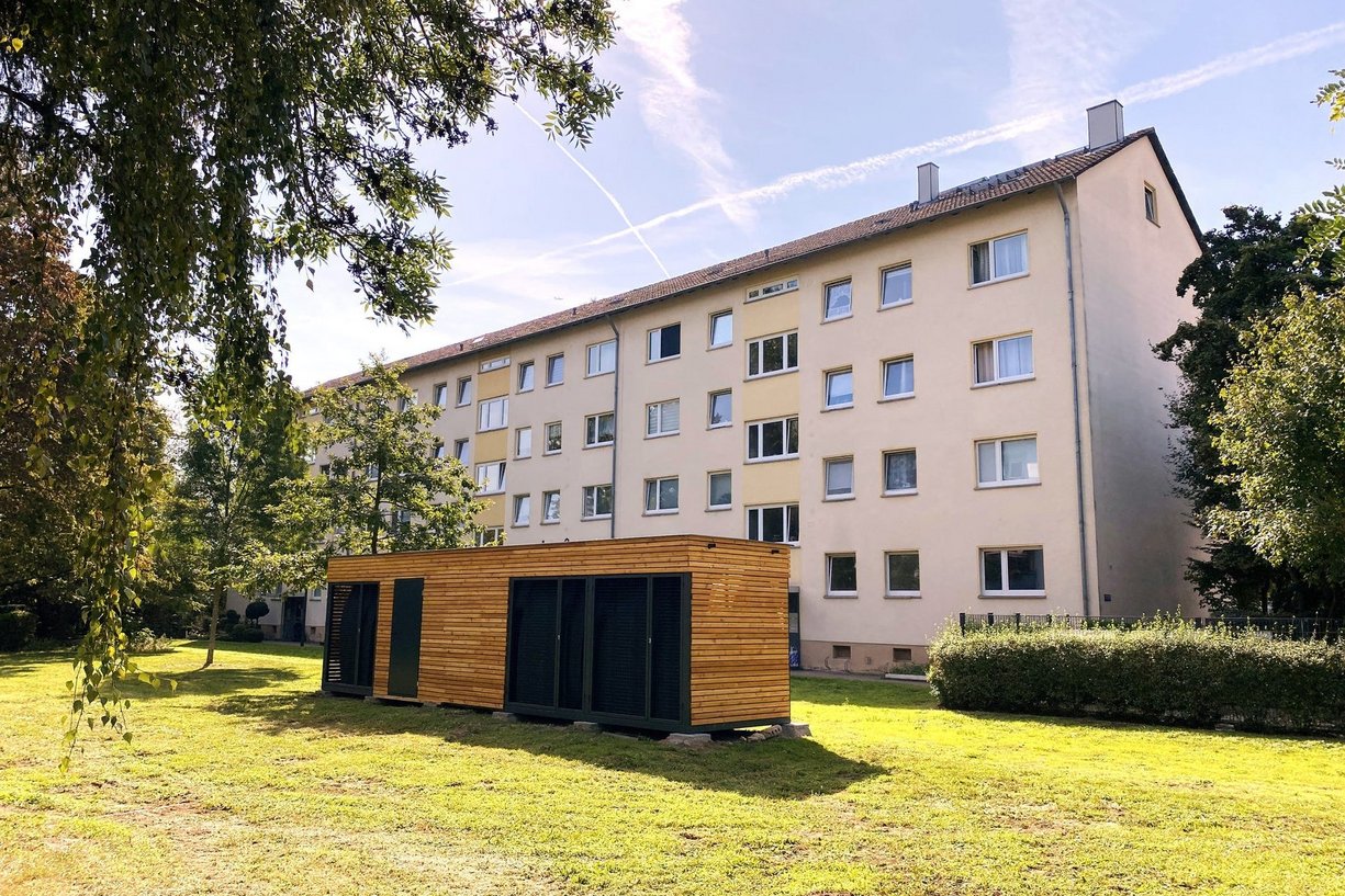 DAIKIN Energiemodul vor Bestandsgebäude. Bild zeigt Container eines Energiemoduls auf grüner Wiese vor einem Mehrfamilienhaus.