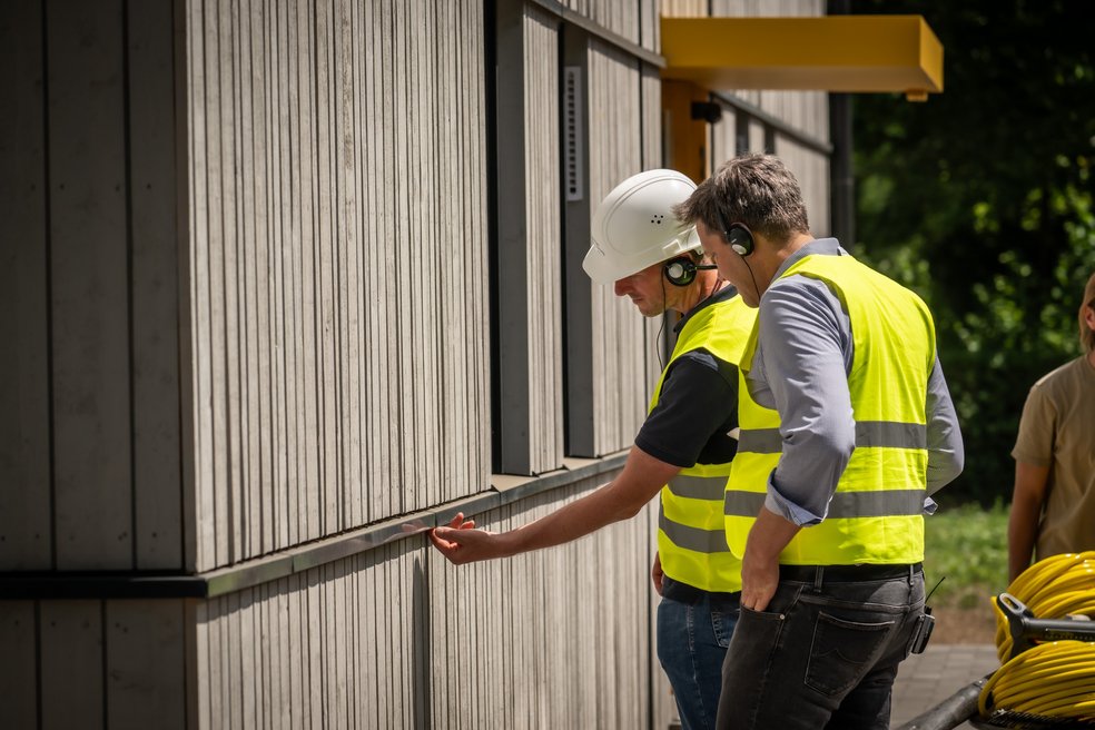 Zwei Personen schauen sich eine Hausfassade prüfend an.