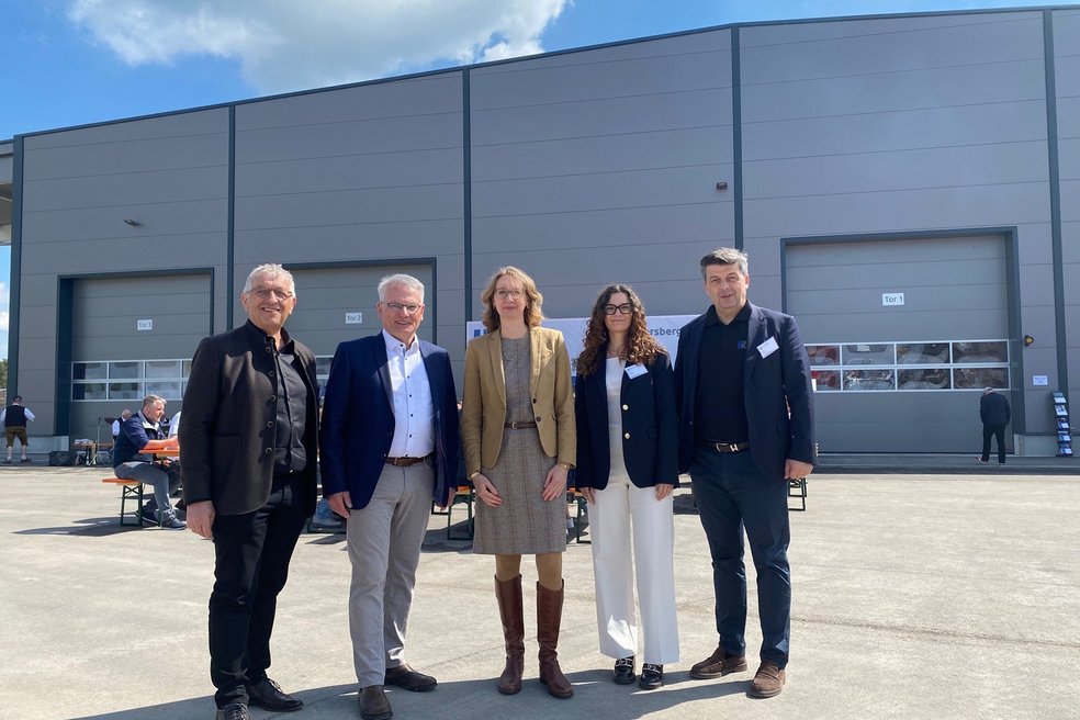 Fünf Personen stehen nebeneinander für ein Gruppenbild vor einer neuen Produktionshalle.