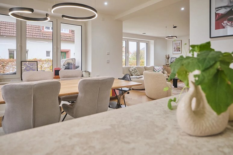 Blick von der Küche in einen hellen, modern gestalteten Eß- und Wohnbereich mit großer Fensterfront