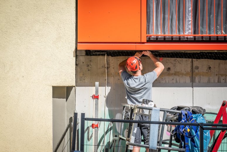 Bauarbeiter montiert vorgefertigtes Element an eine Fassade.