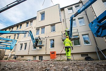 Arbeiter bringen per Kran vorgefertigte Fassadenteile an Gebäude an