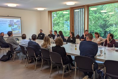 Personen sitzen an einem großen weißen Tisch in einem Raum mit großem Fenster.