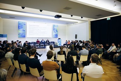 Publikum sitzt auf Stühlen bei einer Panel-Diskussion und schaut zur Bühne.