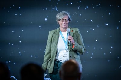 Person steht mit Mikrofon in der Hand vor Publikum.