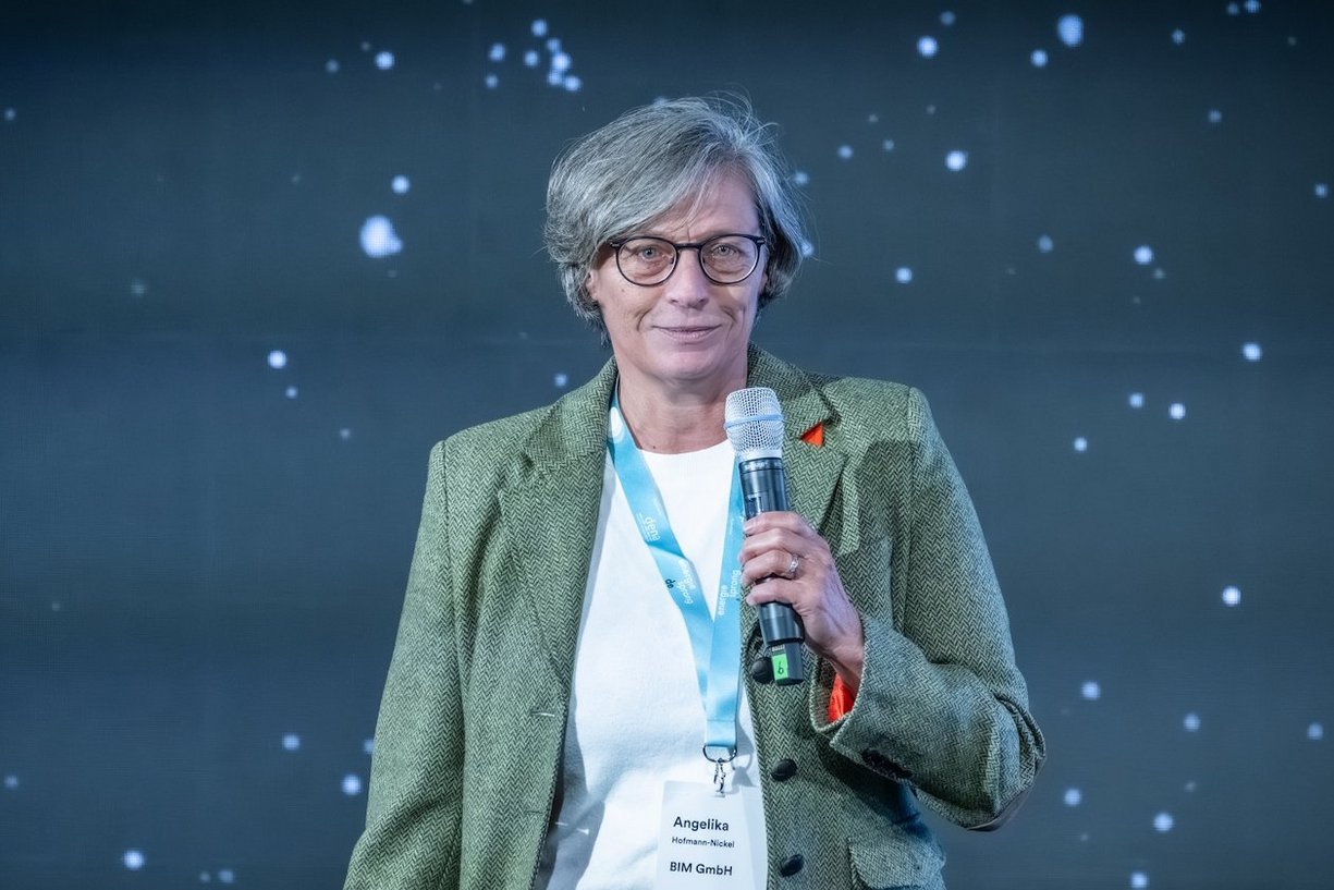 Person steht mit Mikrofon in der Hand vor Publikum.