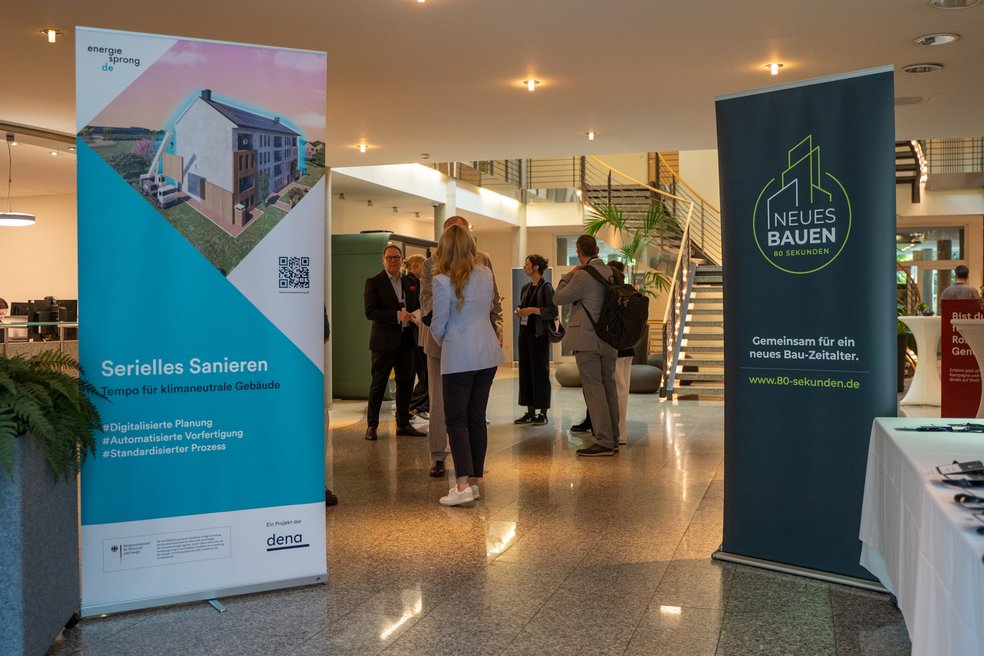 Foyer mit zwei Aufstellern (Energiesprong DE, Neues Bauen) und Personen in Gesprächen