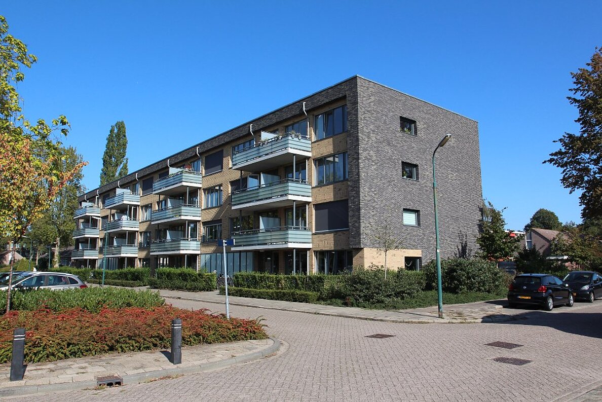 Saniertes Wohnhaus mit Balkonen, davor eine kleine Straße und Grünanlagen