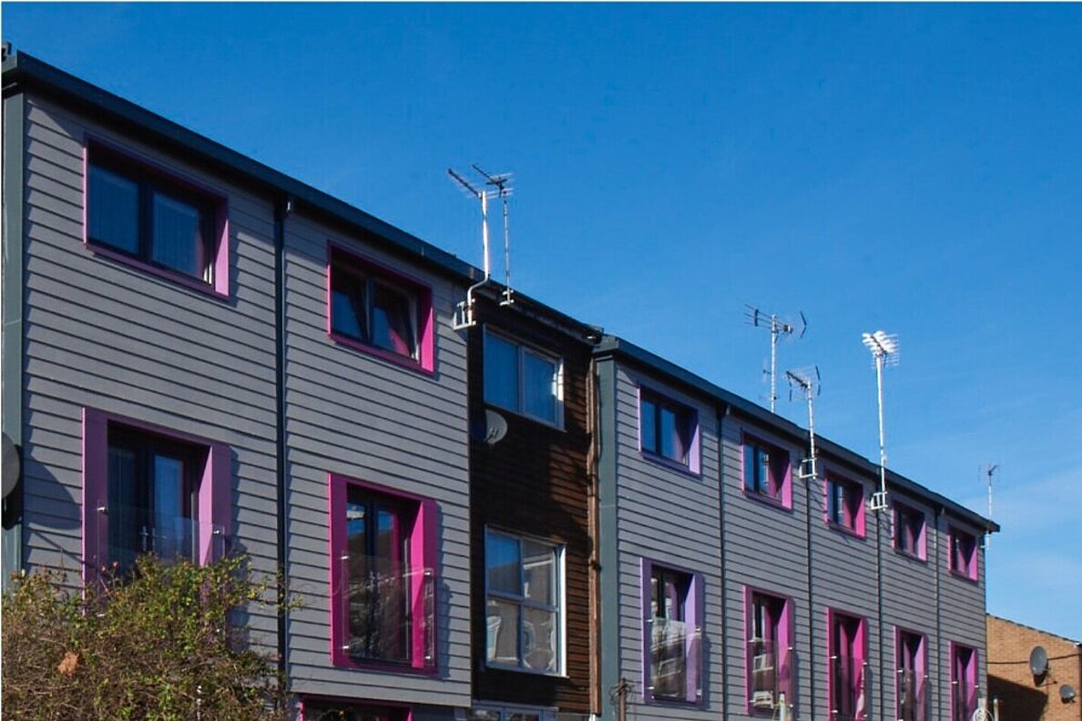 Wohnhaus nach der Sanierung mit grauer Fassade und Fensterrahmen in Pink und Lila