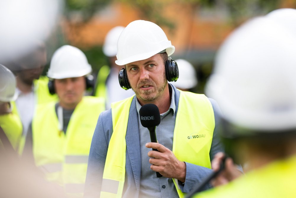 Martin Scholz, Niersberger Building Solutions Person mit gelber Warnweste und Helm auf dem Kopf sowie Mikrofon in der Hand
