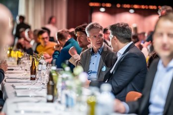 Personen in Business-Kleidung sitzen an einem langen, gedeckten Tisch.
