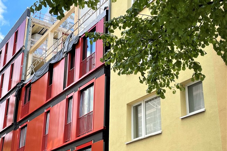 Fassade von zwei aneinandergrenzenden Wohngebäuden. Das Gebäude linksseitig wird mit roten Fassadenelementen saniert.