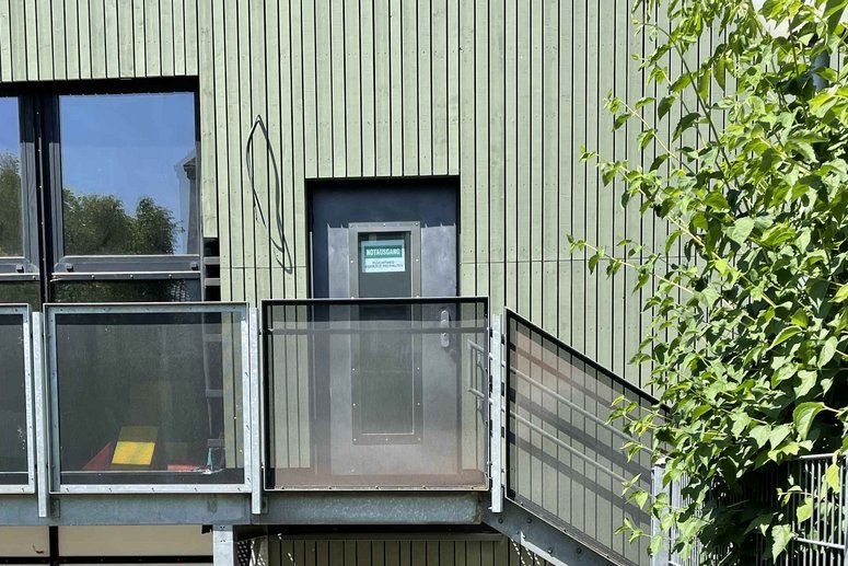 Zugang in ein Gebäude mit hellgrüner Holzfassade über eine Treppe von außen