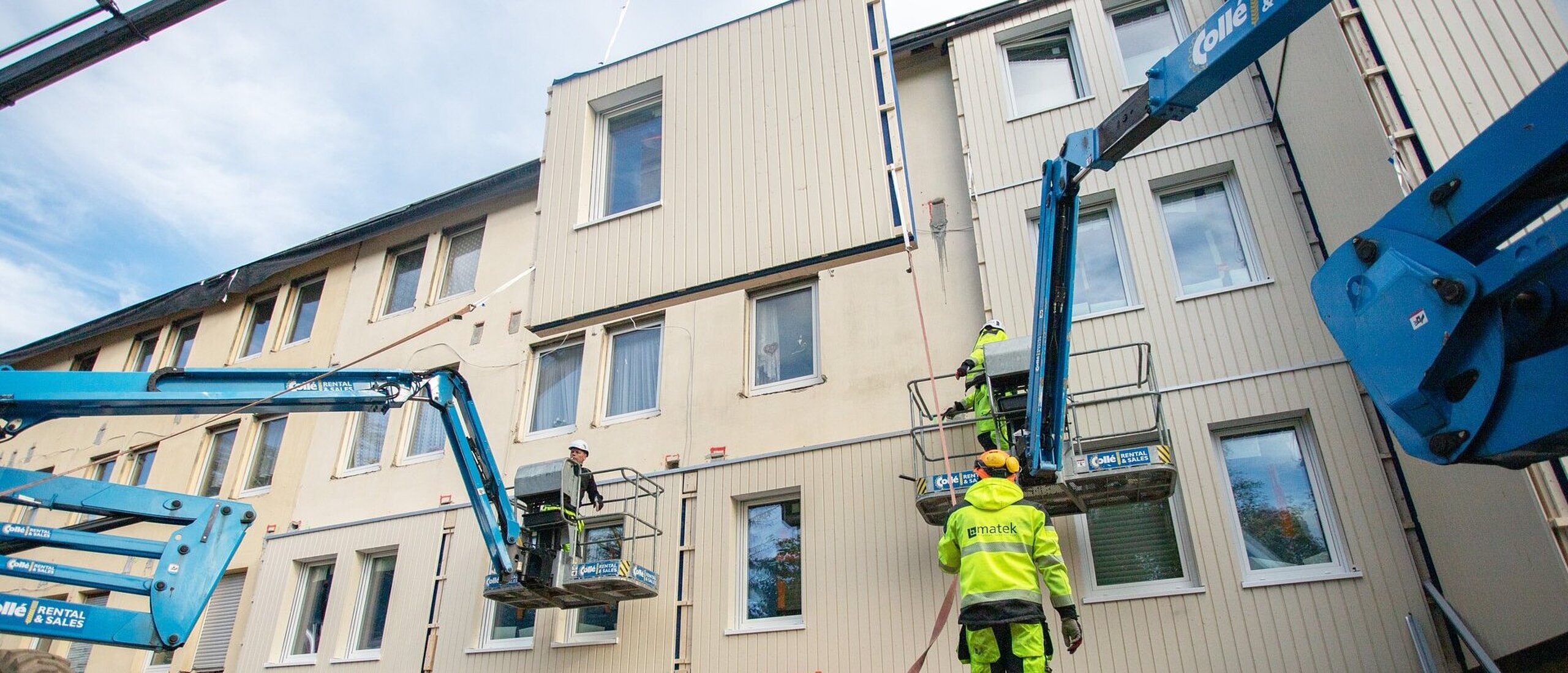 Kran mit Arbeitern vor Hausfassade in Sanierung