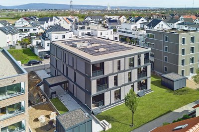 Bild zeigt Draufsicht eines neugebauten Mehrfamilienhauses mit PV-Anlage auf dem Dach von anderen Häusern umringt