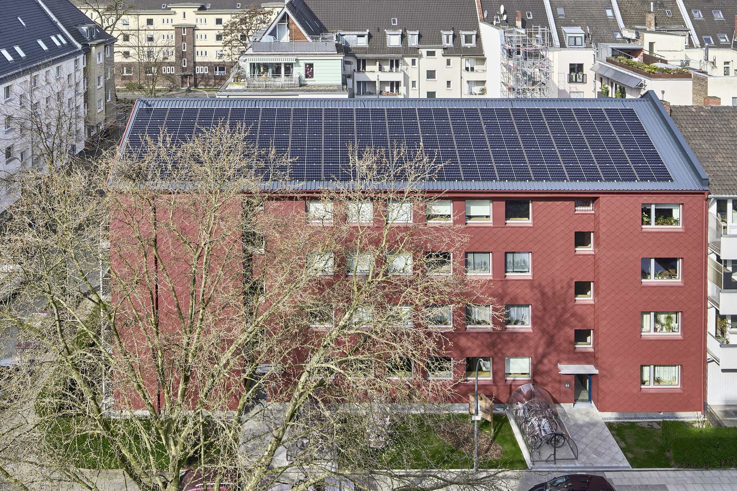 Fertig saniertes Wohnhaus mit einer Fassade aus roten Alu-Rauten, auf dem Dach Solarmodule