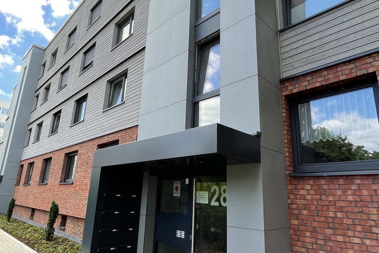Moderner Eingangsbereich zu einem neu sanierten Wohngebäude, davor Fußweg