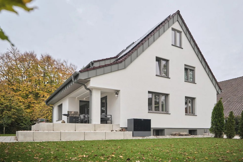 Einfamilienhaus nach der Sanierung, helle Putzfassade, Schrägdach , davor Rasenfläche