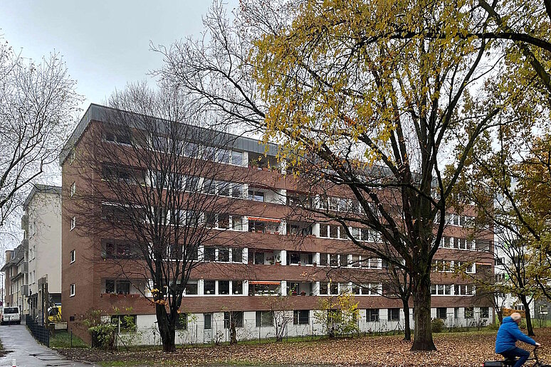 Mehrfamilienhaus fünfgeschossig mit Balkonen und Flachdach, davor Laubbäume