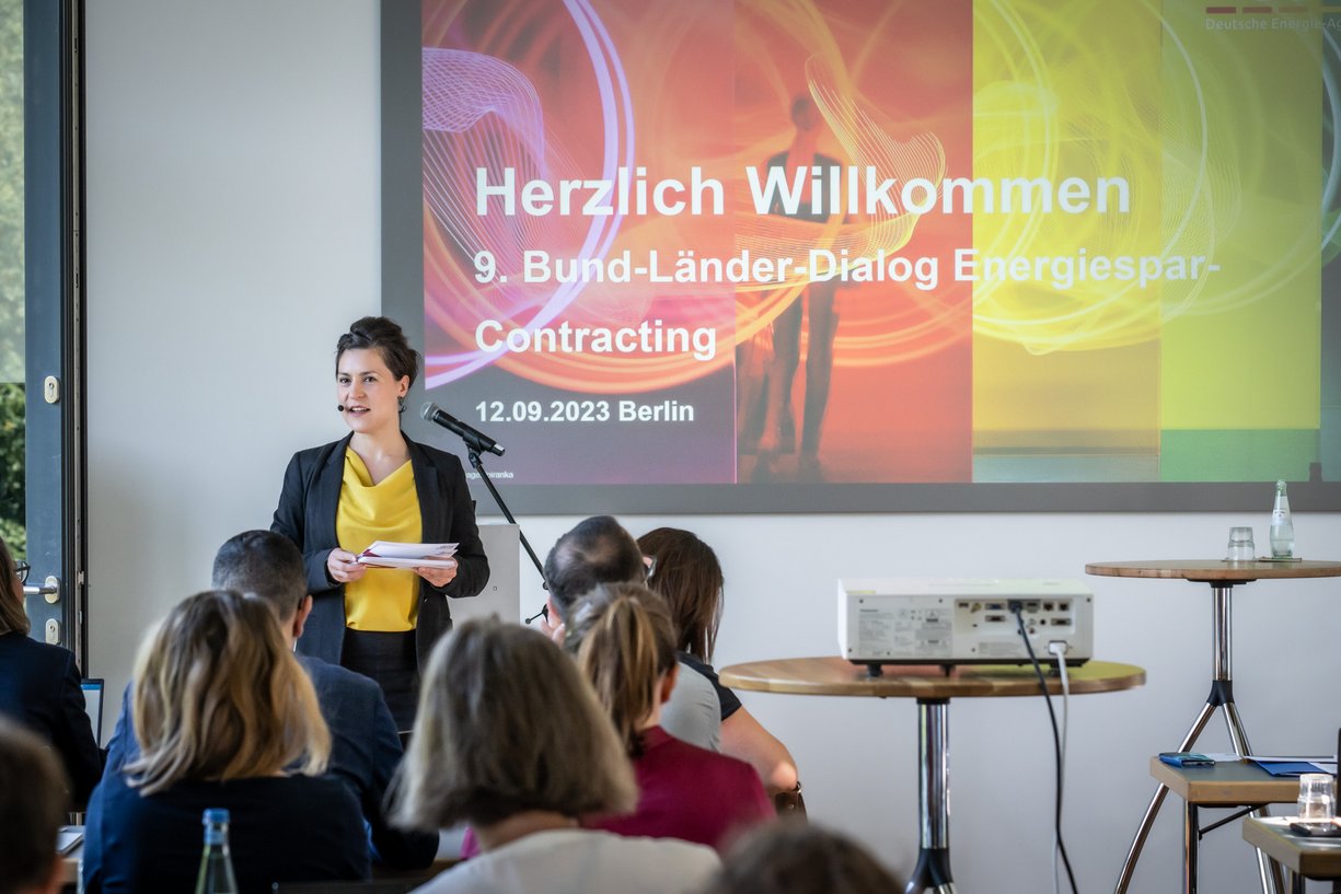 Am 12. September trafen sich rund 40 Verantwortliche aus Bund, Ländern und Kommunen zum Austausch über das zukunftsweisende Energiedienstleitungskonzept in Berlin. Vortragende vor Leinwand