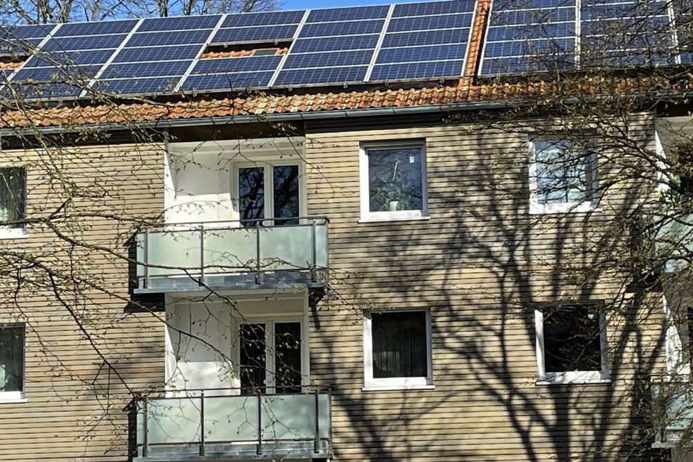 Photovoltaikanlagen auf dem Dach liefern klimaneutralen Strom für Erdwärmepumpen, die Geothermie in Heizenergie umwandeln. Mehrfamilienhaus mit Holzfassade und PV-Anlage auf dem Dach