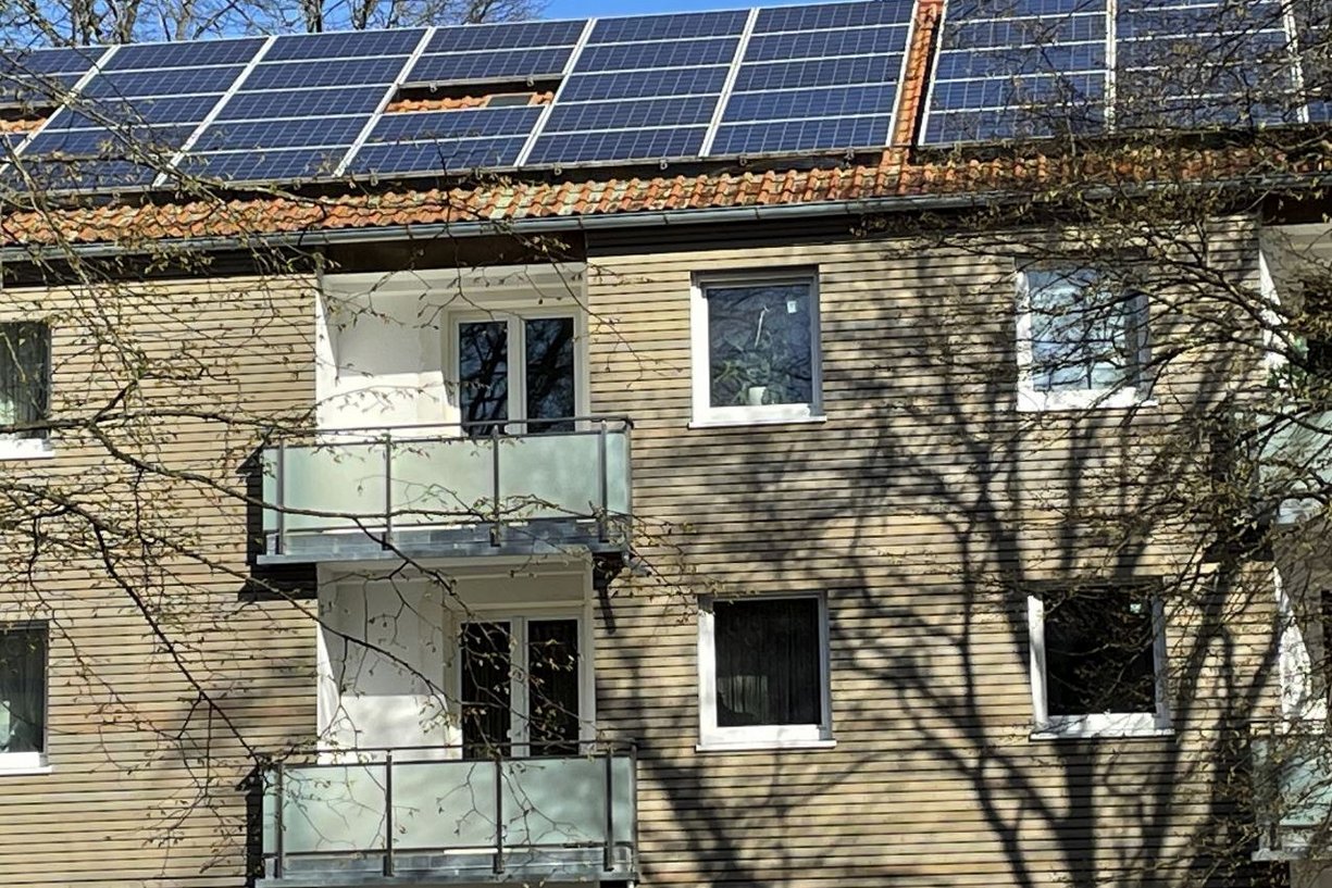 Photovoltaikanlagen auf dem Dach liefern klimaneutralen Strom für Erdwärmepumpen, die Geothermie in Heizenergie umwandeln. Mehrfamilienhaus mit Holzfassade und PV-Anlage auf dem Dach