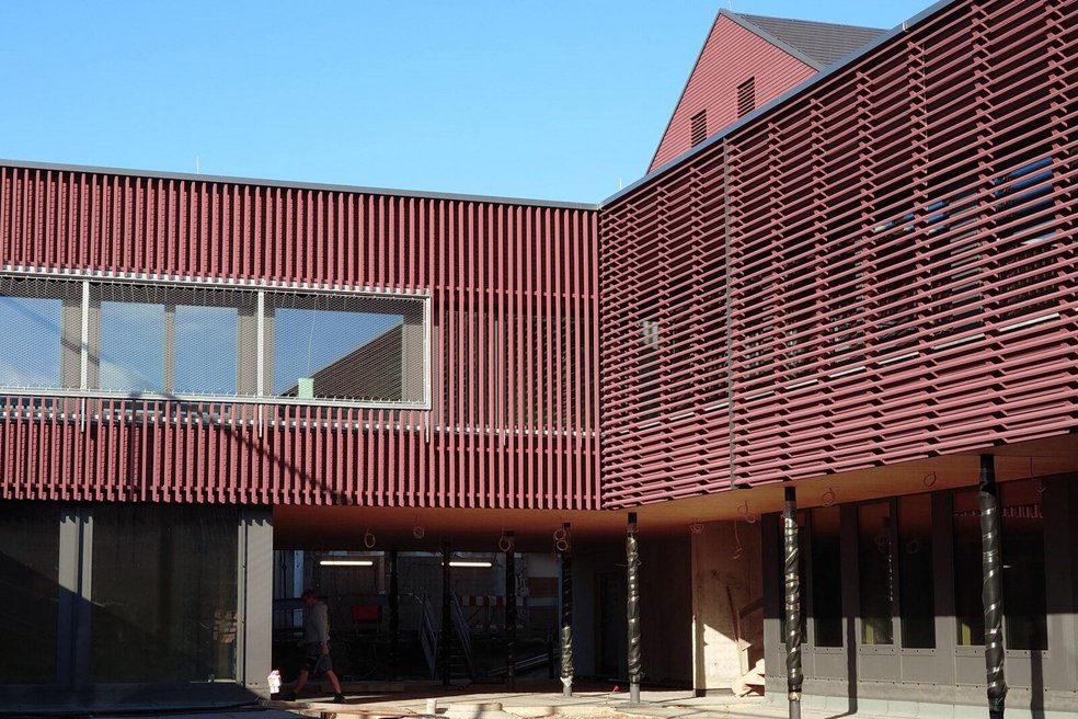Teil eines Schulgebäudes mit rötlicher Fassade, im Hintergrund blauer, wolkenloser Himmel