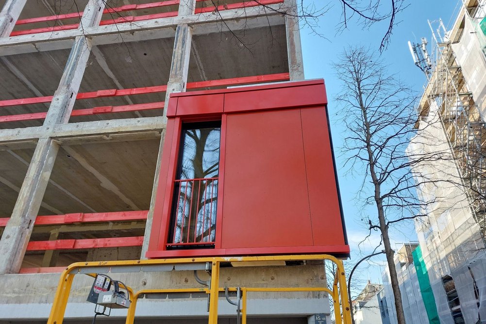 Vorgefertigtes Fassadenelement Fassadenelement (rot) wird an Gebäude platziert.