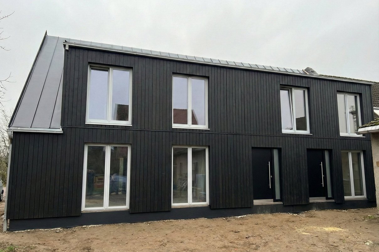 Bild zeigt Ansicht eines Hauses mit neuer Fassade in dunklem Holz mit großen Fenstern