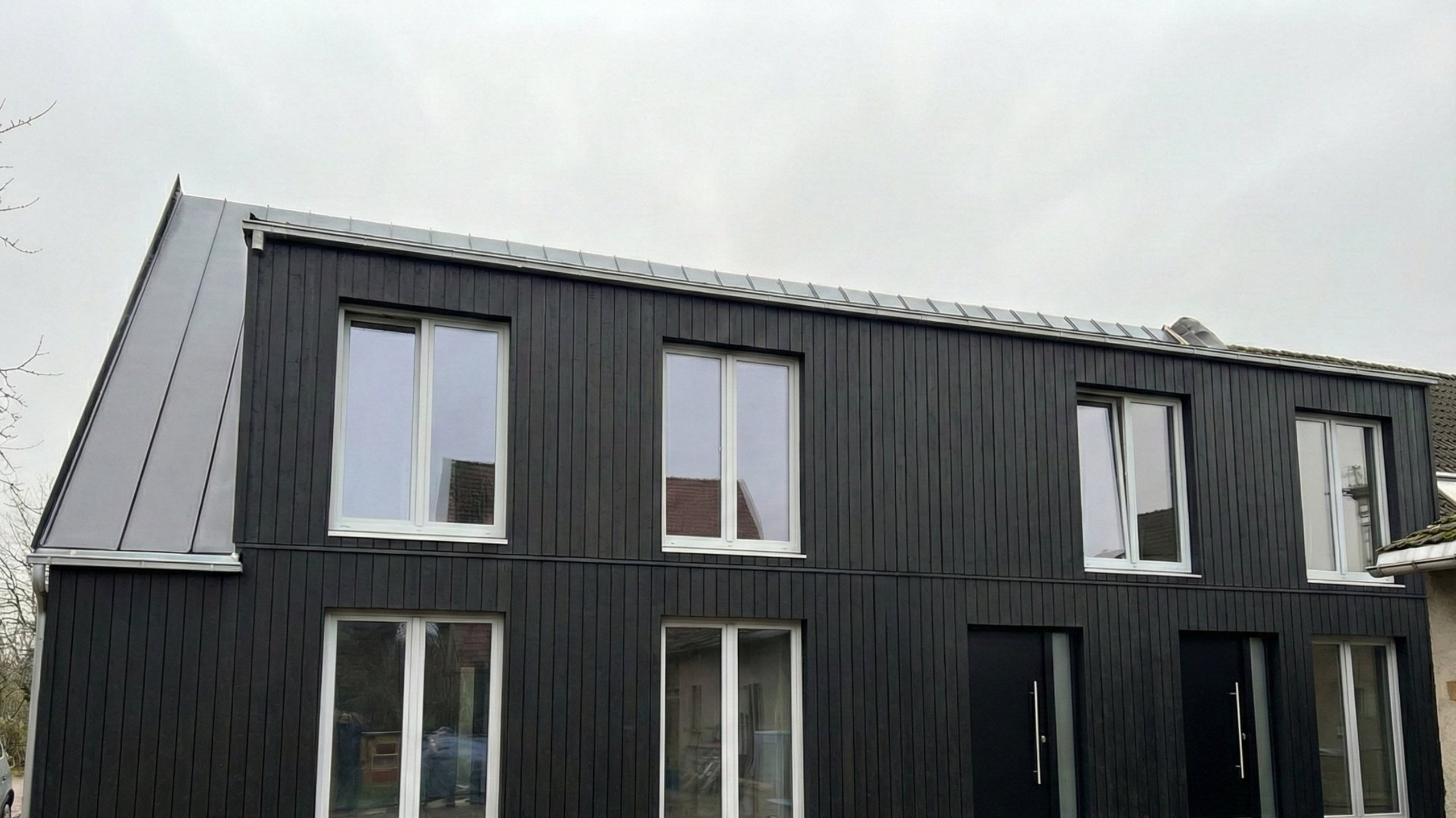 Bild zeigt Ansicht eines Hauses mit neuer Fassade in dunklem Holz mit großen Fenstern