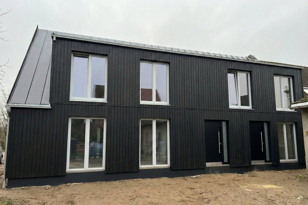 Bild zeigt Ansicht eines Hauses mit neuer Fassade in dunklem Holz mit großen Fenstern