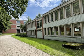 Gebäude mit großen Fenstern, zweigeschossig, unsaniert, davor Rasenfläche und ein Weg