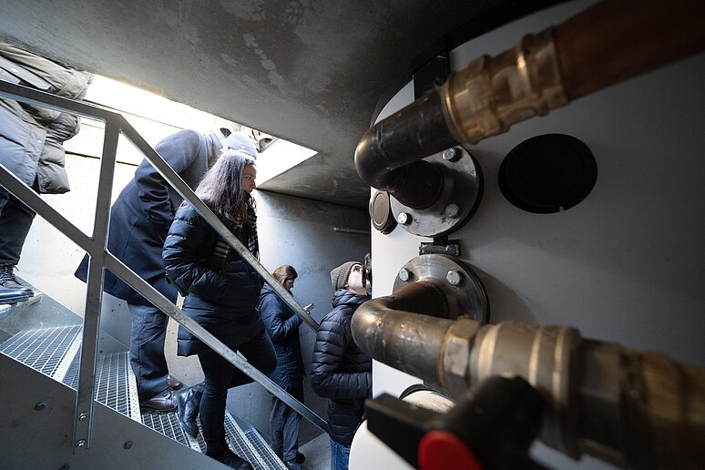 Personen steigen eine Treppe in den Untergrund hinab,  Rohre an den Wänden