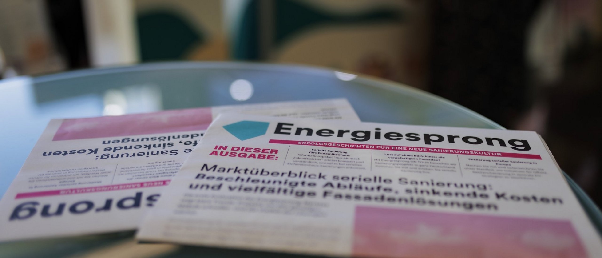 Zwei Energiesprong Zeitungen liegen auf einem rundem Glastisch.