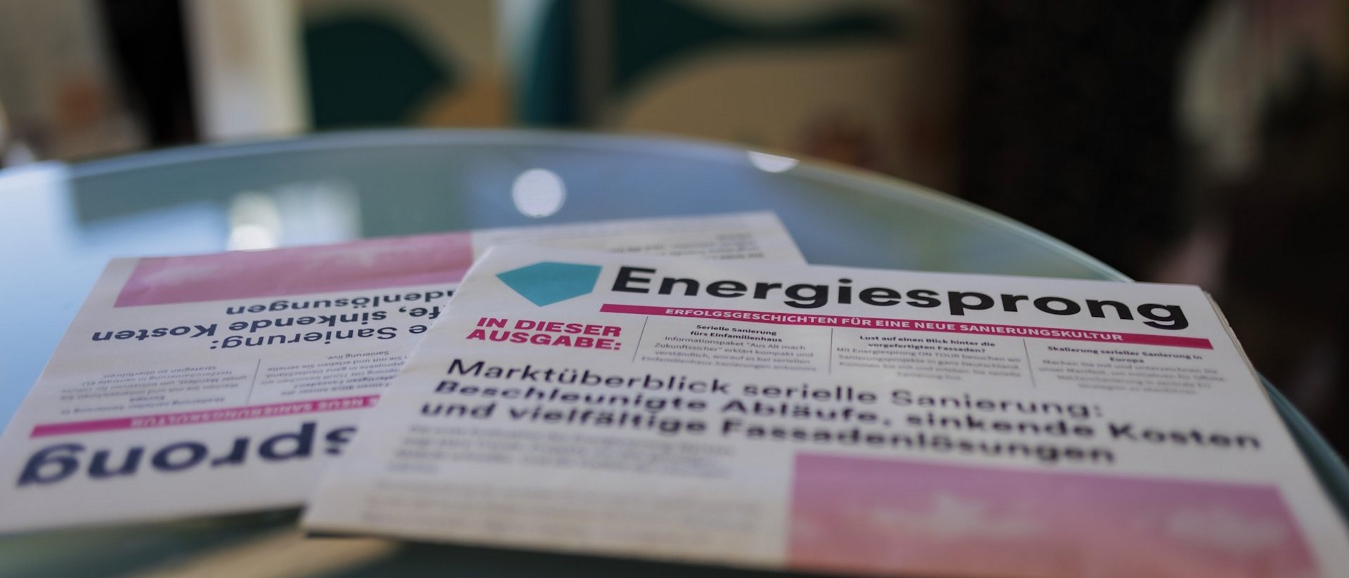 Zwei Energiesprong Zeitungen liegen auf einem rundem Glastisch.
