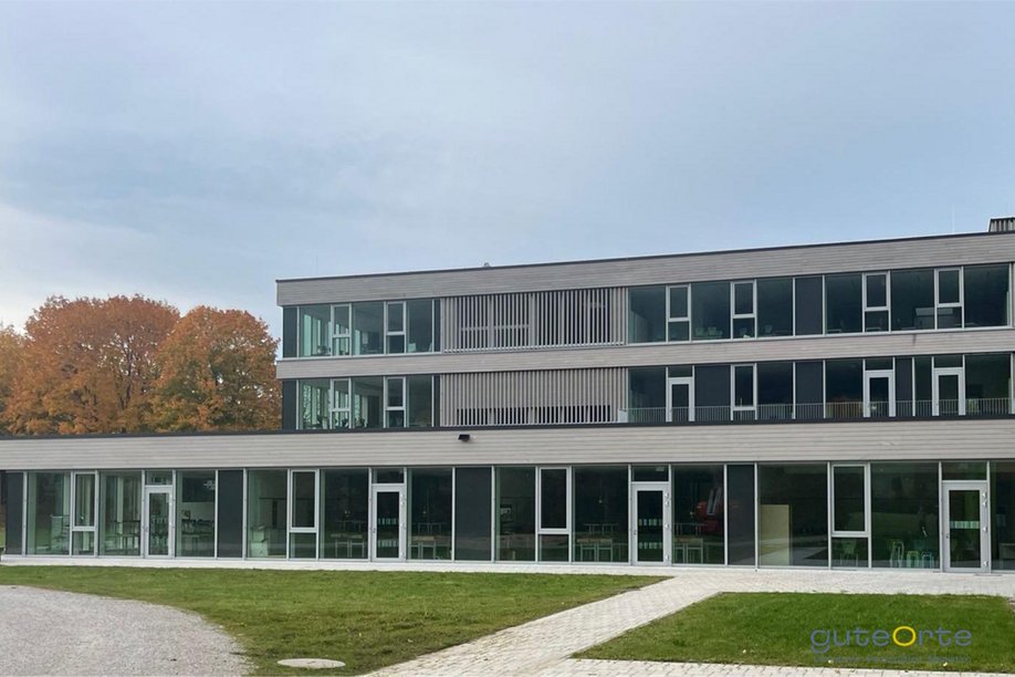 Modernes Schulgebäude dreigeschossig, davor Rasenflächen und Wege