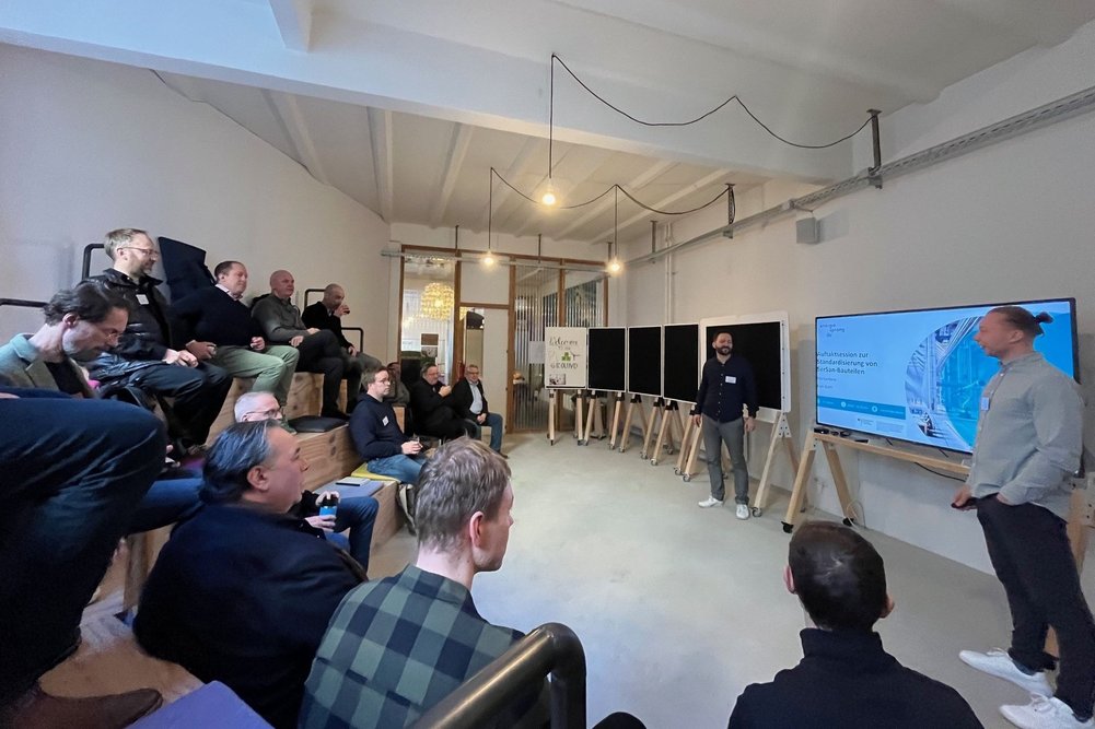 Moderiert wurde der Tag von den Energiesprong-Teammitgliedern Elia Cardone, depact GmbH und Kian Giahi. Zwei Personen stehen neben einer Präsentationsfläche.