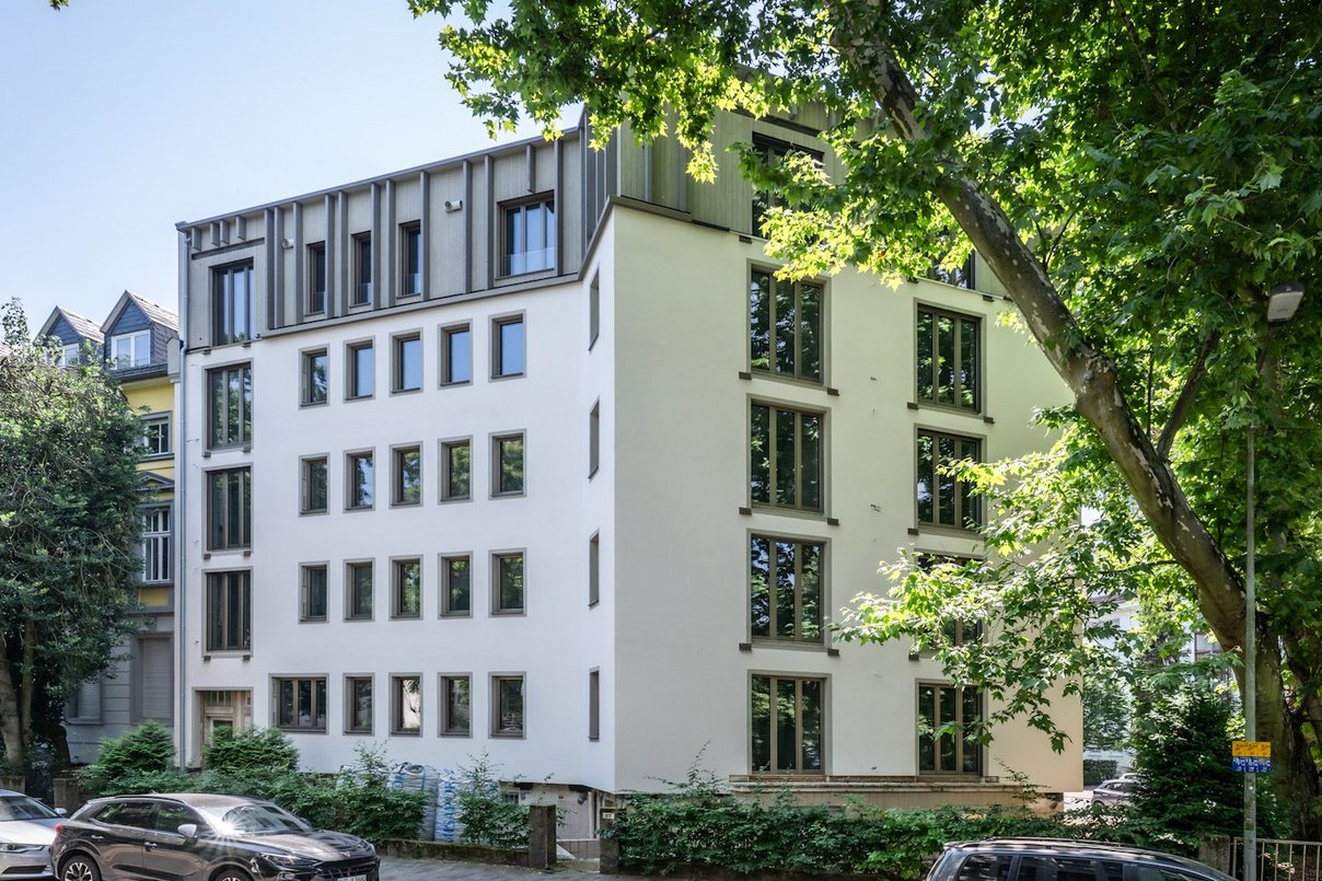 Mehrfamilienhaus fünfgeschossig mit Fenstern, davor Straße mit parkenden PKWs