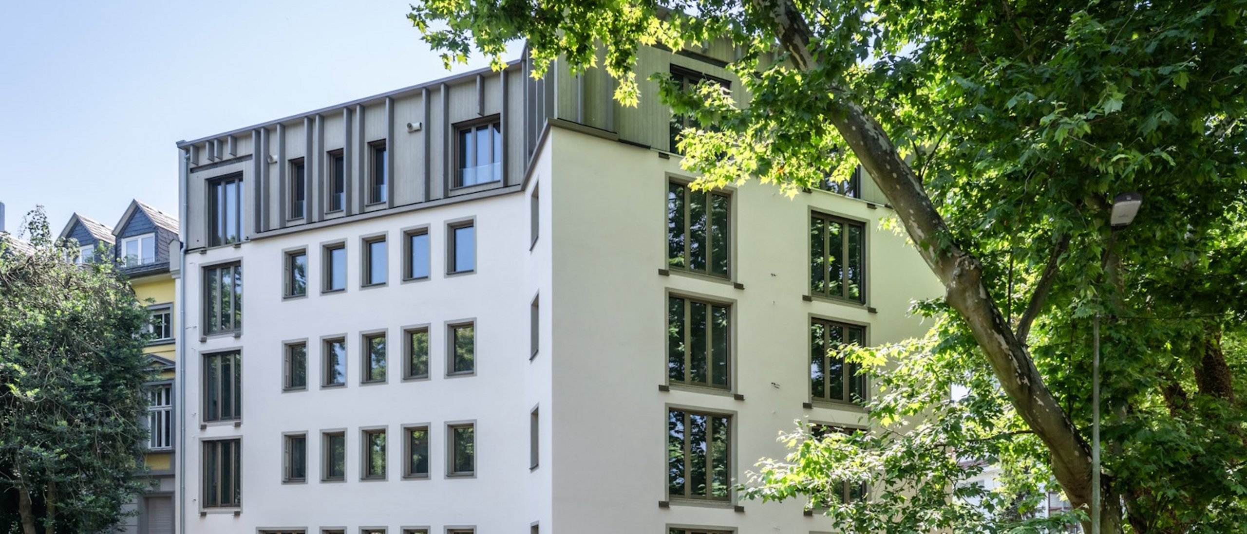 Mehrfamilienhaus fünfgeschossig mit Fenstern, davor Straße mit parkenden PKWs