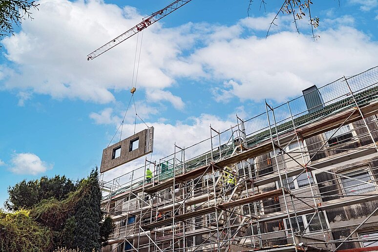 Fliegende Fassadenelemente mit Kran vor Baustelle