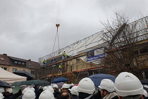 Menschen mit Bauhelmen vor Baustelle und Kran