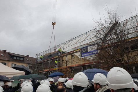 Menschen mit Bauhelmen vor Baustelle und Kran