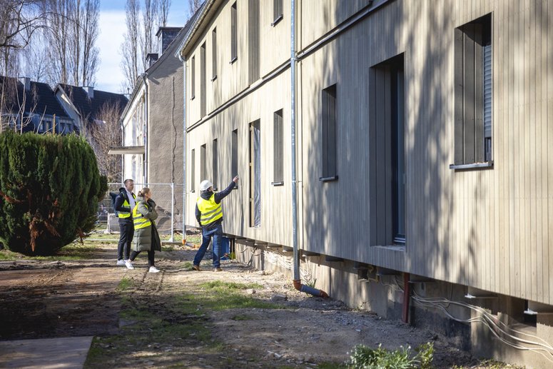 Drei Personen stehen vor einem neu sanierten Mehrfamilienhaus und begutachten die Fassade.