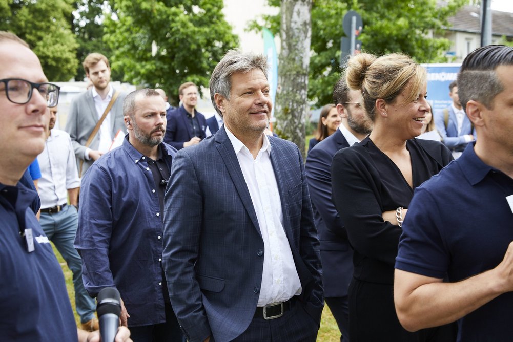 Bundeswirtschaftsminister Robert Habeck bei seinem Besuch der Baustelle in Mönchengladbach im Juli 2023 gemeinsam mit Mona Neubaur (Wirtschaftsministerin NRW). Mehrere Personen dunkel gekleidet auf einer Baustelle